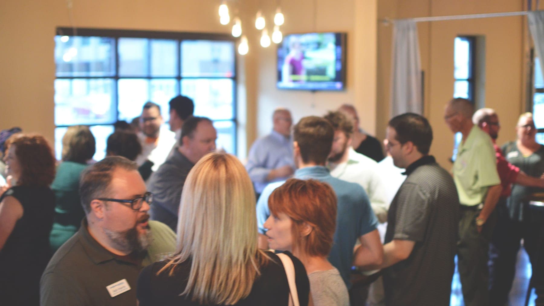 A crowded room of guests mingling in conversation at a Drinking Lunch networking event in Lansing, Michigan, with Ash Harris among them.